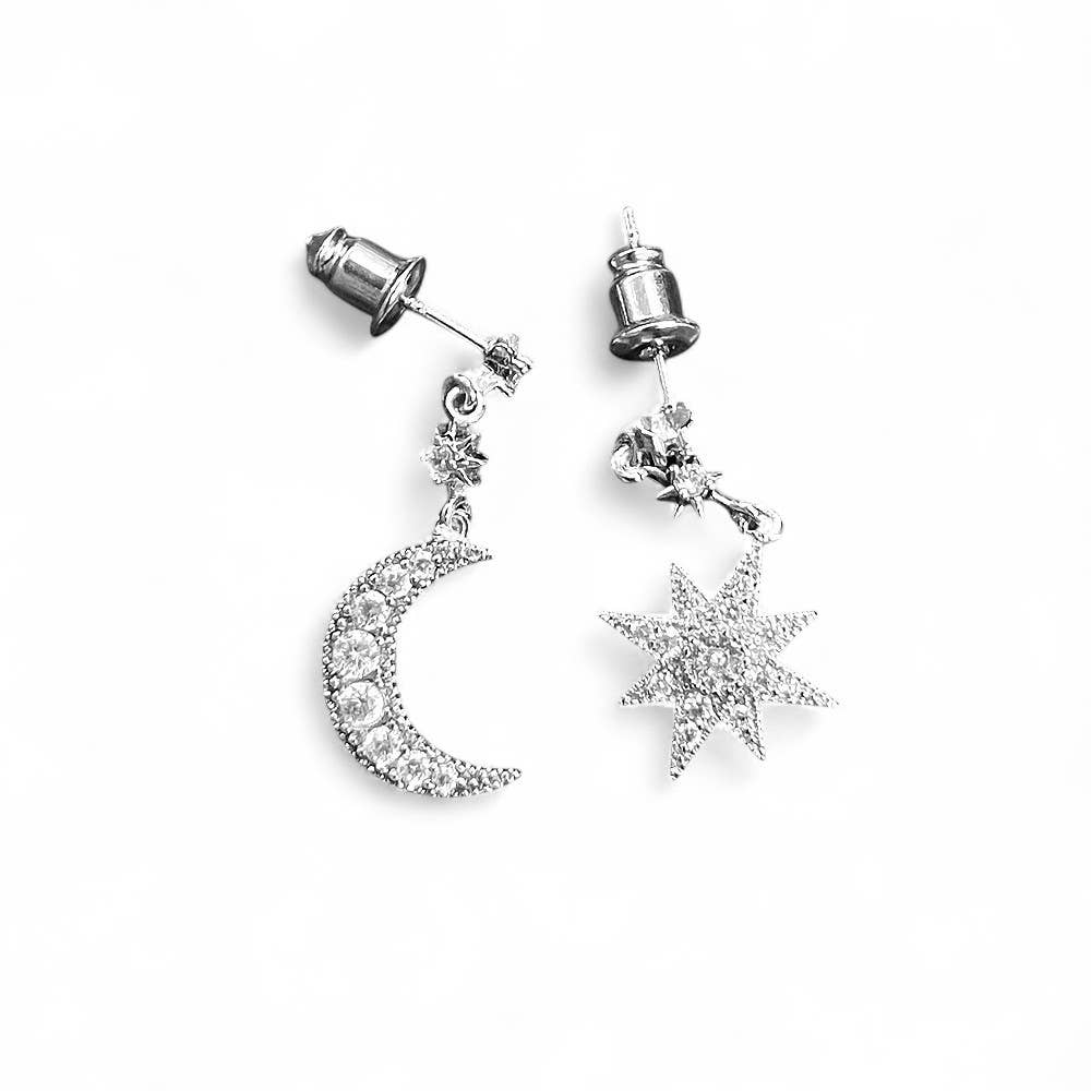 Silver earrings with moon and star designs on a white background