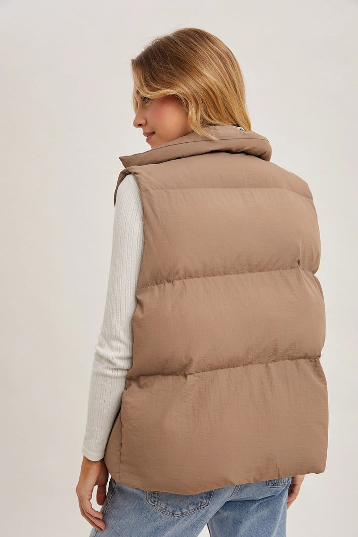 Woman wearing a beige puffer vest on a plain background