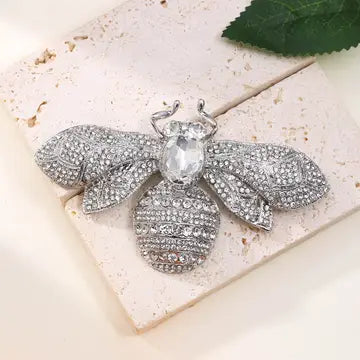 Silver bee-shaped brooch with gemstones on a stone surface