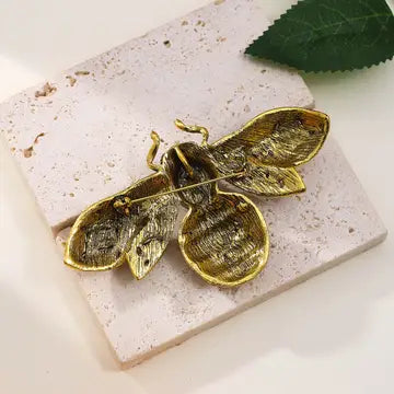 Gold bee-shaped brooch on a stone surface with a leaf