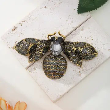 Decorative brooch shaped like a bee with gemstone body on a textured surface