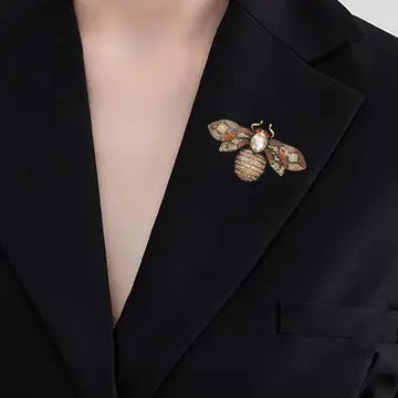 A close-up of a person wearing a black blazer with a gold and brown patterned bee brooch pinned to the lapel.