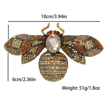 A bee-shaped brooch with gold-tone metal and multicolored rhinestone wings and body, shown with measurement lines and text indicating 10cm width, 6cm height, and 51g weight on a white background.