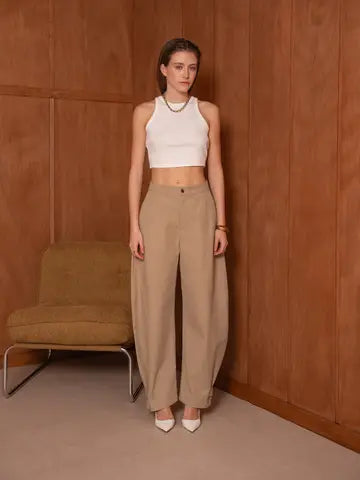Woman wearing a white top and beige pants standing against a brown wall.