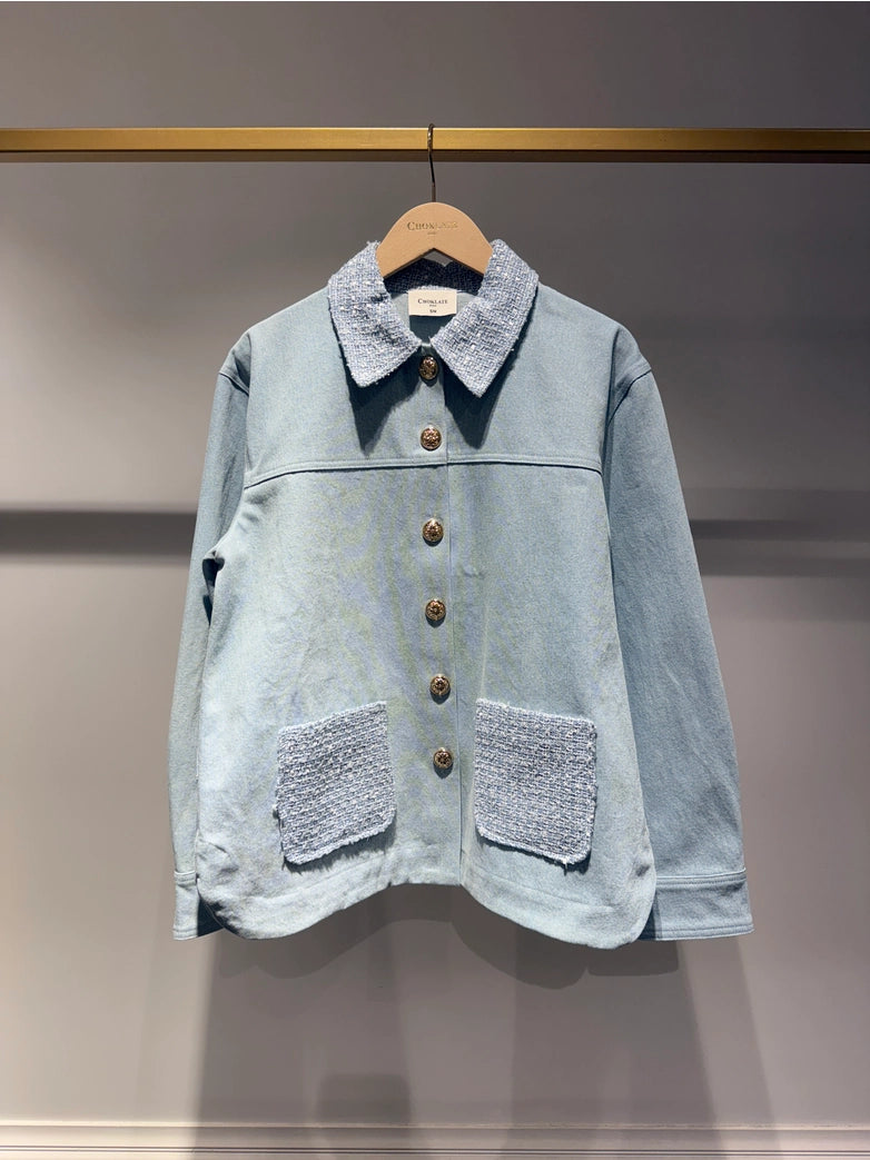 Light blue denim jacket with decorative pockets on a wooden hanger against a neutral background