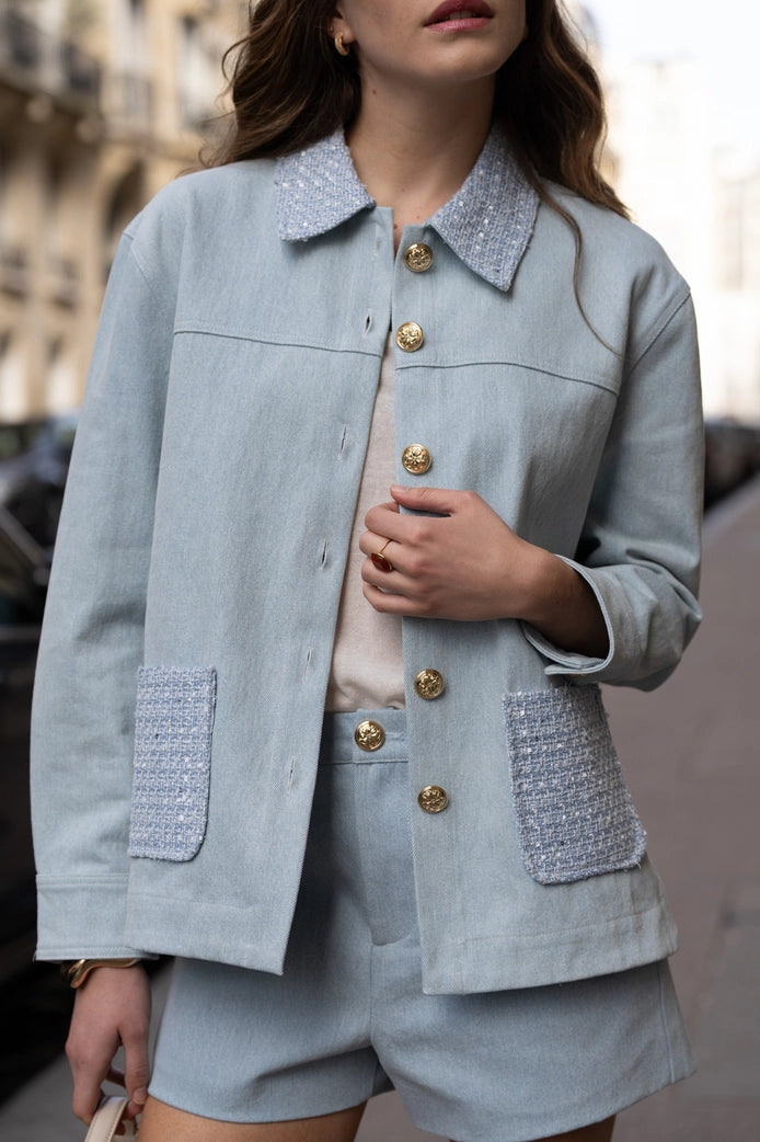 Person wearing a light blue jacket with textured pockets and gold buttons.