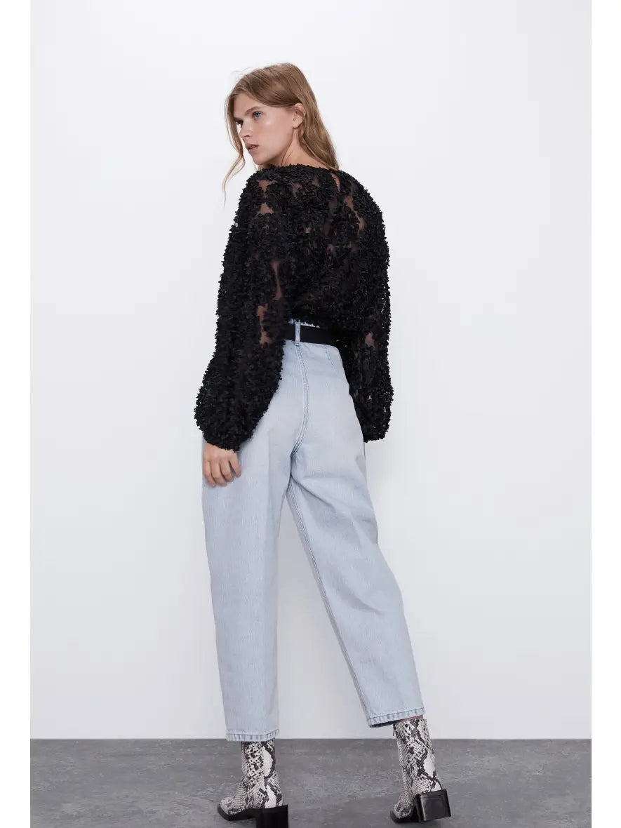 Woman wearing a black textured sweater and light blue jeans against a white background