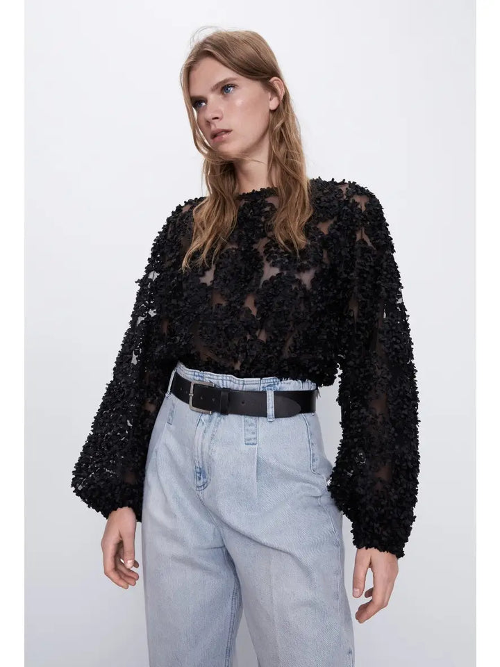 Person wearing a black floral lace top and light blue jeans on a white background
