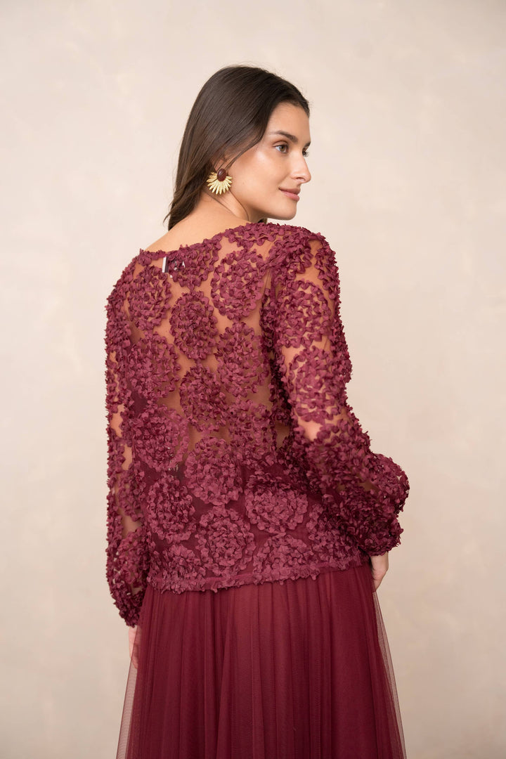 Woman wearing a burgundy lace top and skirt against a beige background