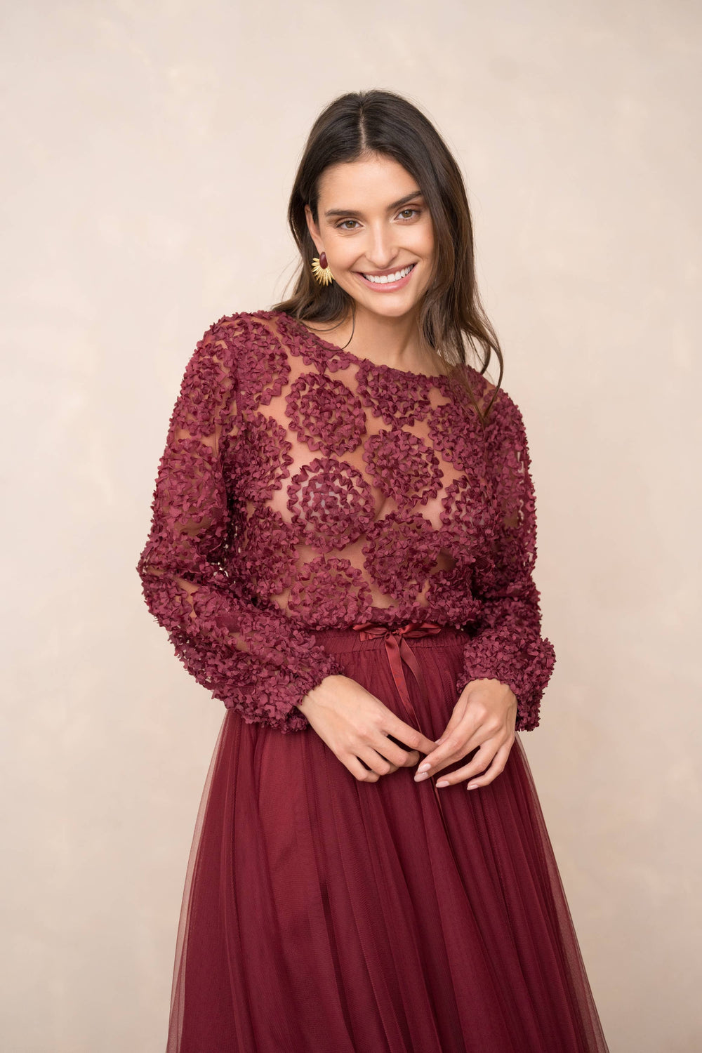 Woman wearing a burgundy lace top and skirt against a beige background