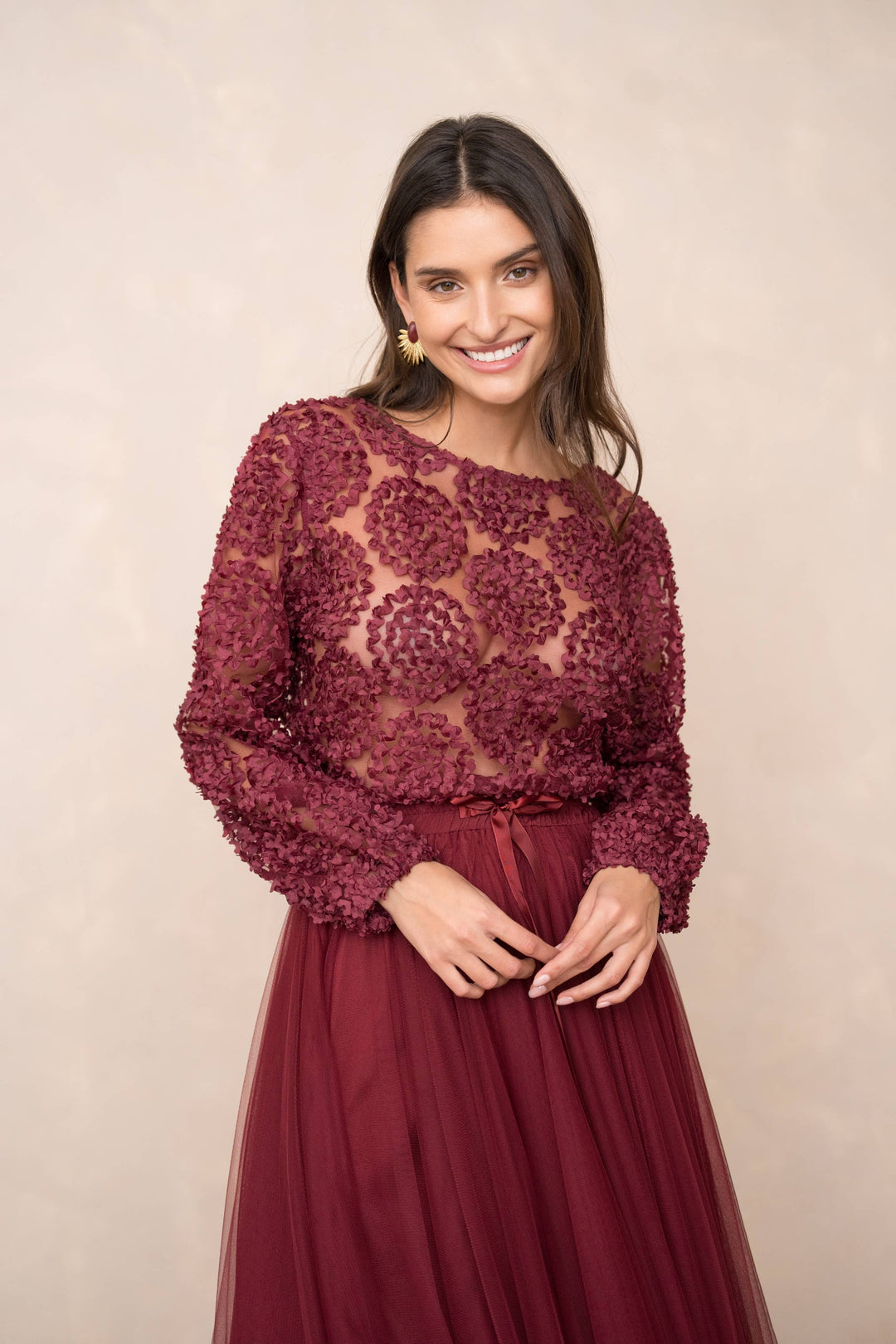 Woman wearing a burgundy lace top and skirt against a beige background