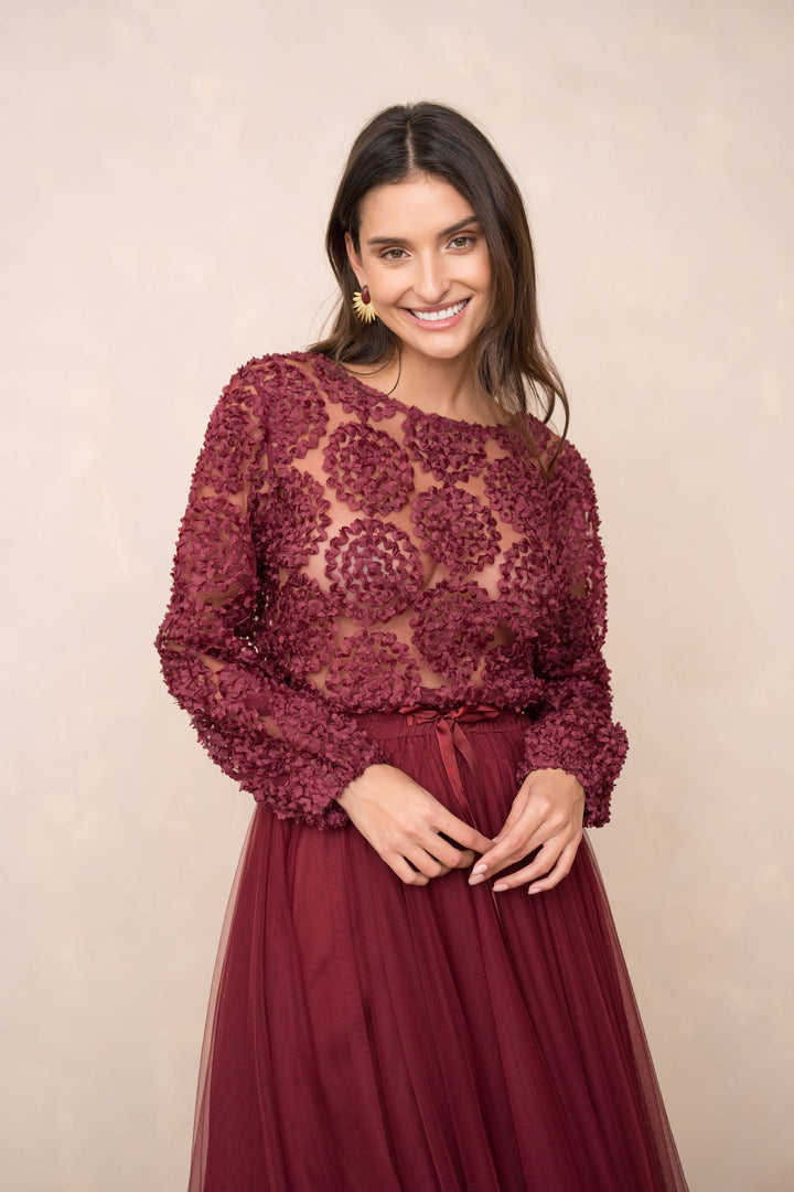 Woman wearing a burgundy lace top and skirt against a beige background