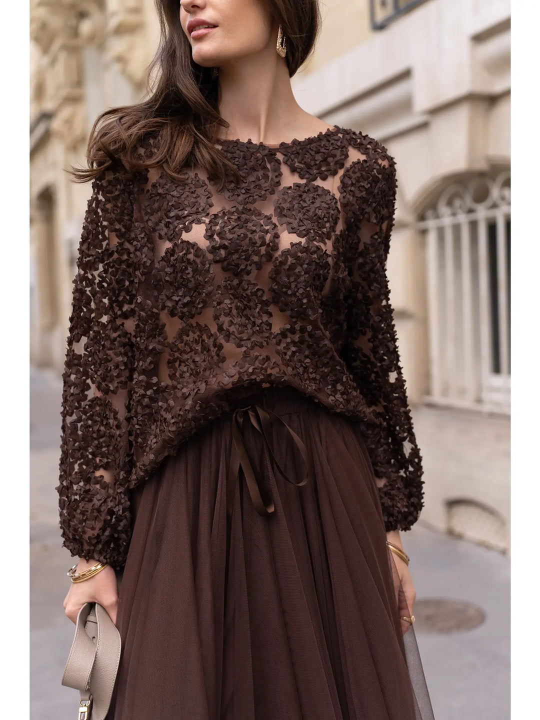 Woman wearing a brown lace top and skirt on a city street.