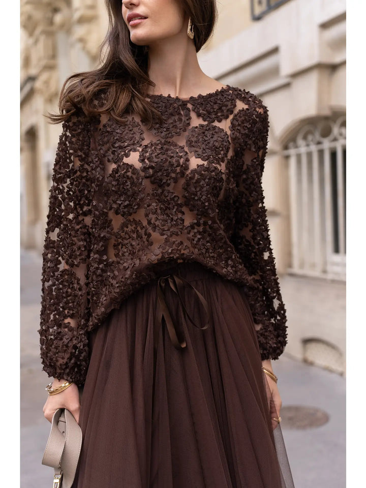 Woman wearing a brown lace top and skirt on a city street.