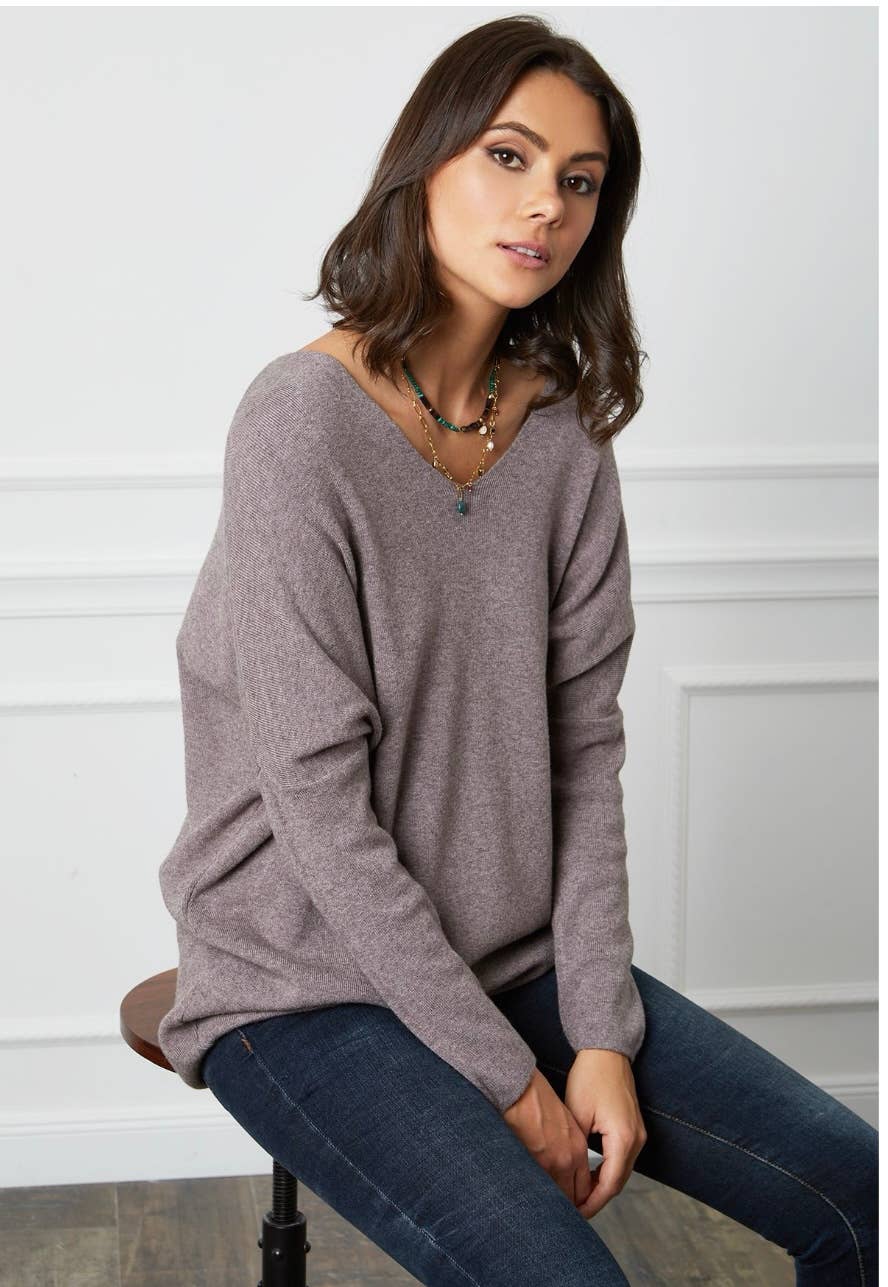 Woman wearing a gray sweater and blue jeans sitting on a chair.