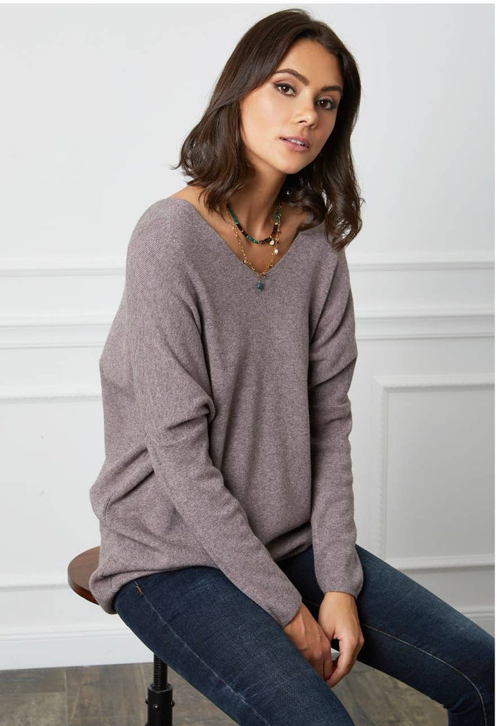 Woman wearing a gray sweater and blue jeans sitting on a chair.