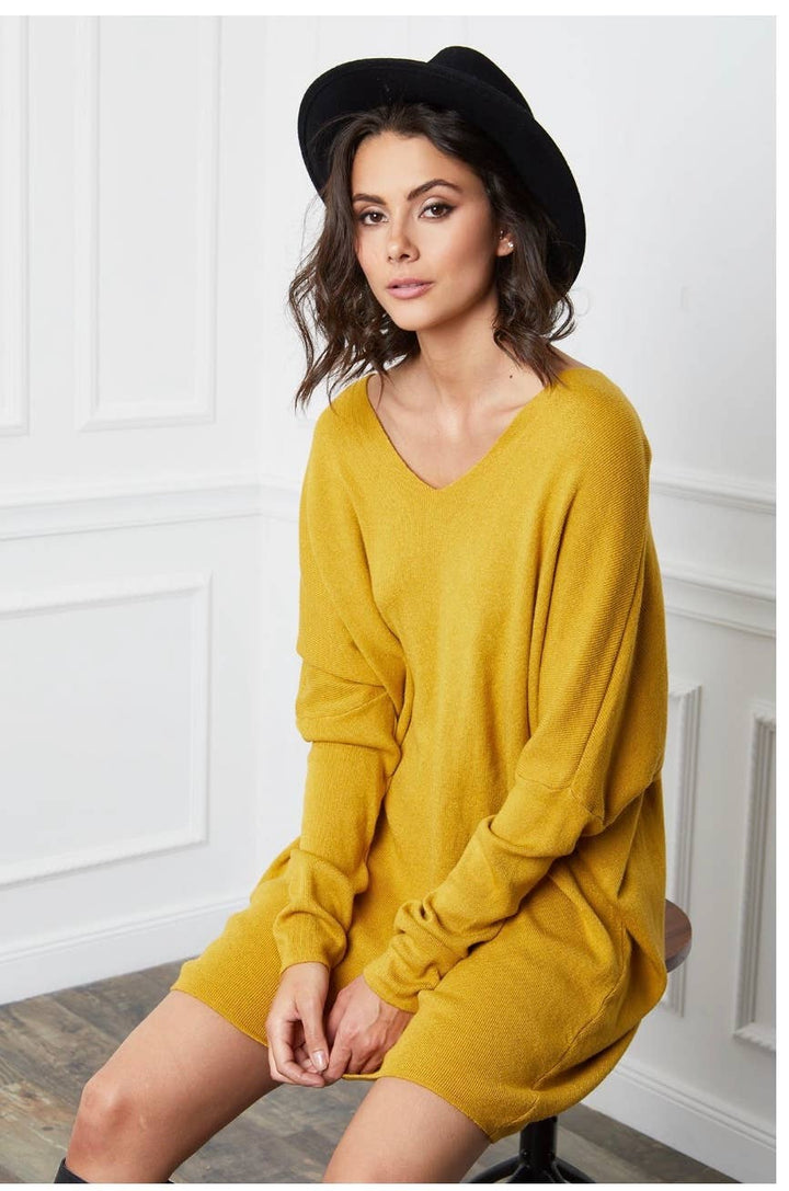 Woman wearing a mustard yellow dress and black hat sitting on a chair.