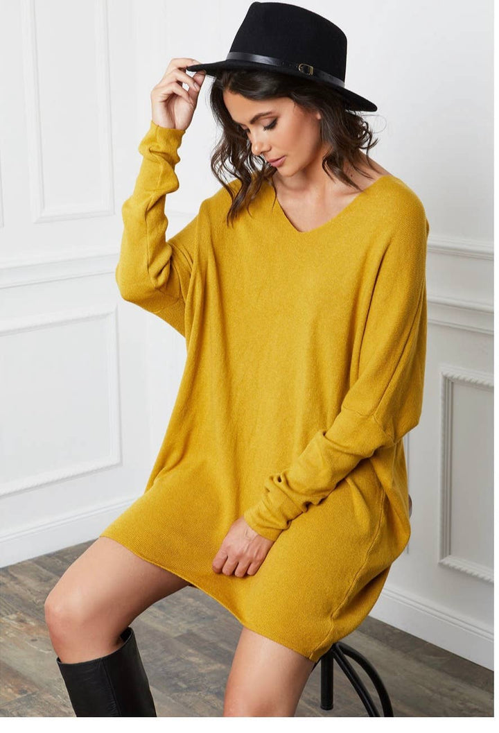 Woman wearing a mustard yellow dress and black hat indoors.