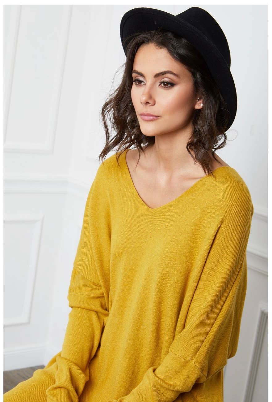 Woman wearing a mustard yellow sweater and black hat against a white background