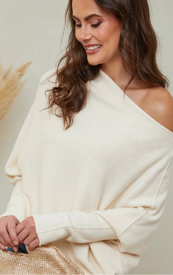 Woman wearing a cream off-shoulder sweater against a neutral background