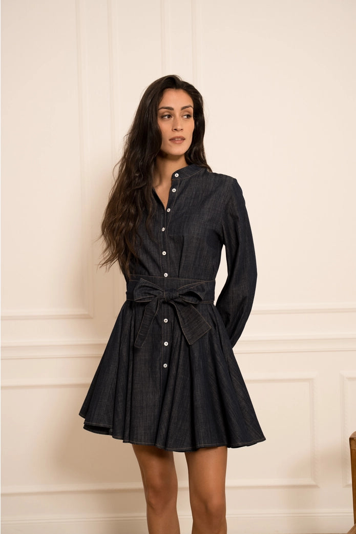 Woman wearing a black dress with a belt against a beige wall.