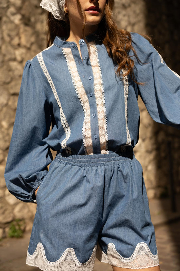 Woman wearing a blue outfit with lace details against a stone wall.