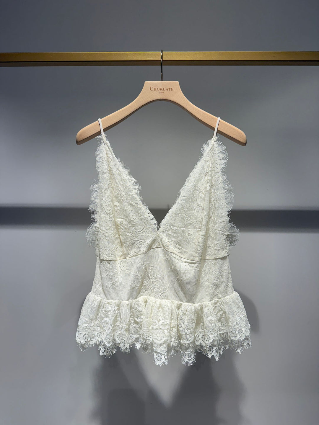 White lace top on a wooden hanger against a gray background