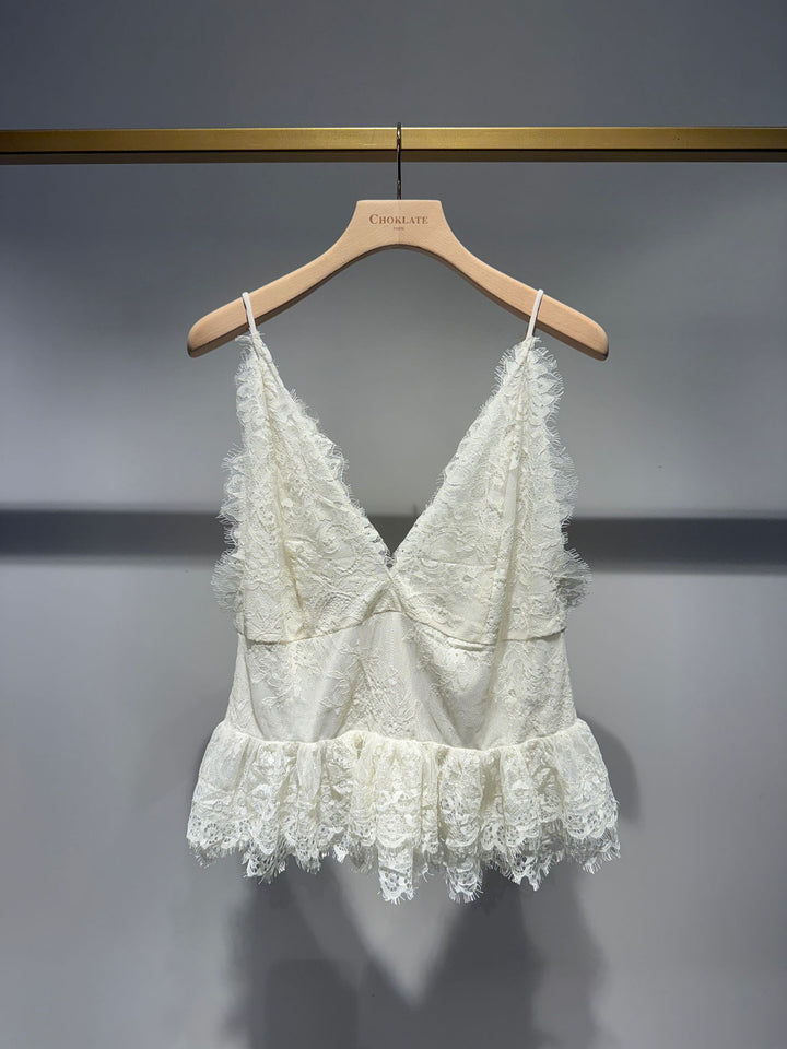 White lace top on a wooden hanger against a gray background