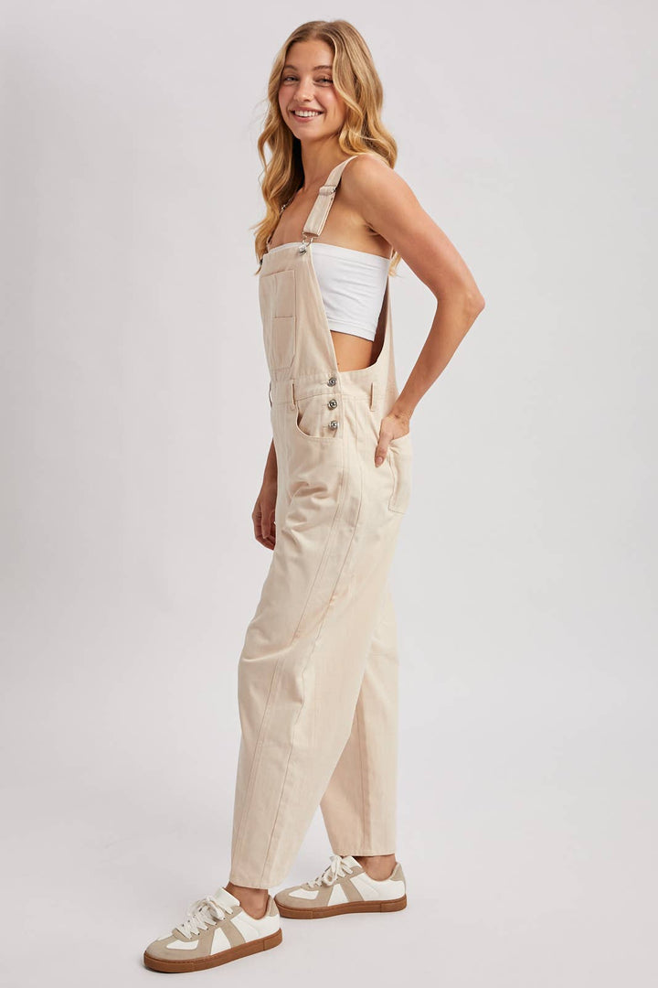 Woman wearing beige overalls and white sneakers on a plain background