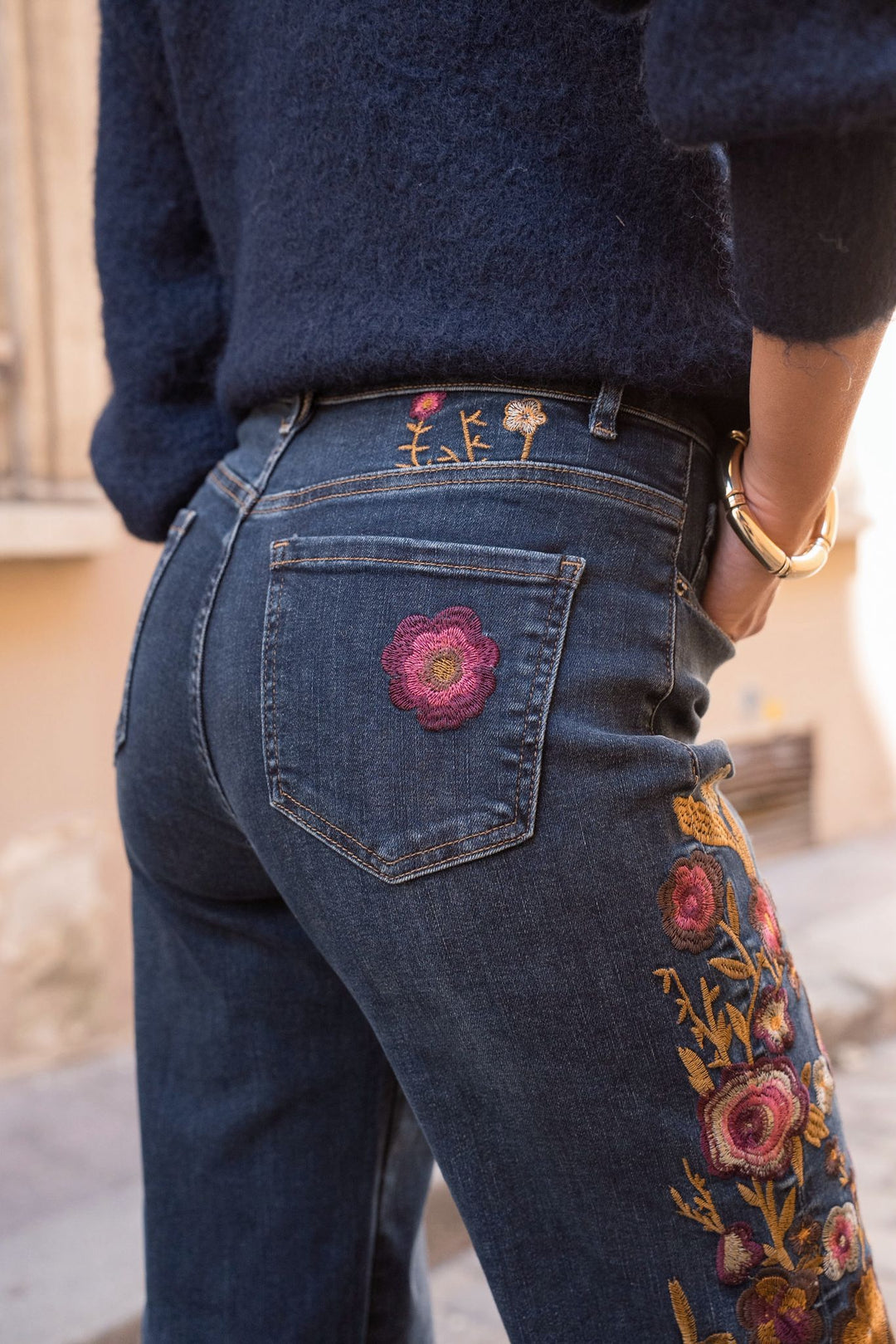 Person wearing blue jeans with floral embroidery, standing outdoors.