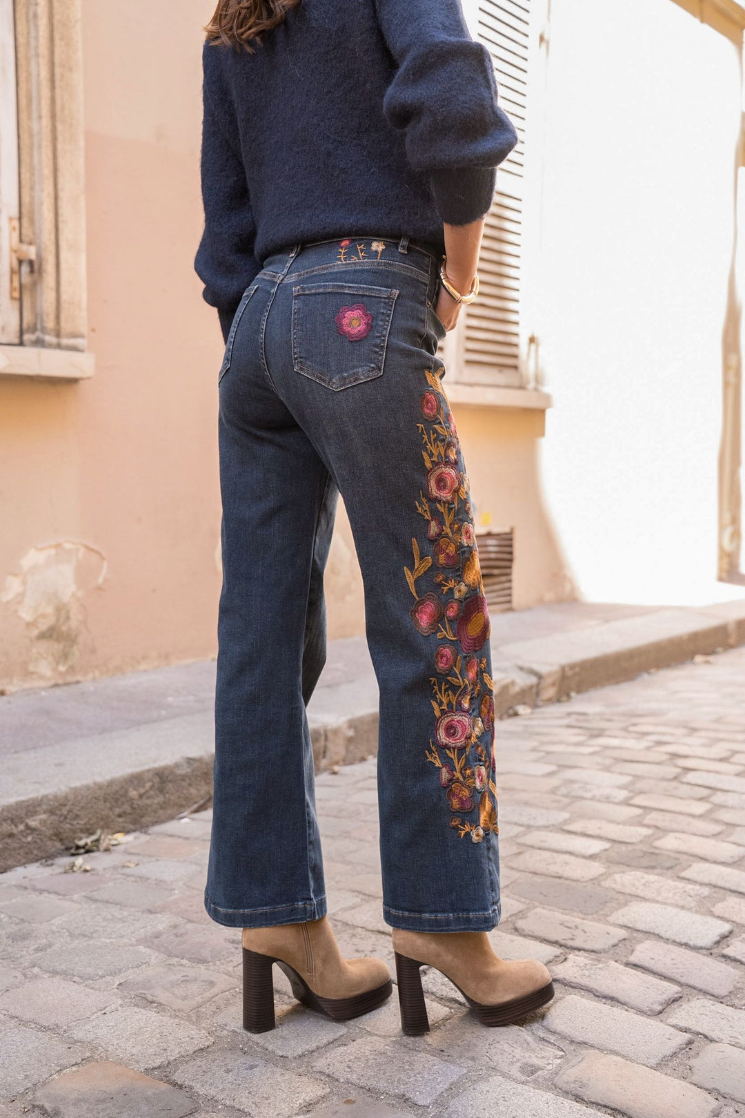Person wearing blue jeans with floral embroidery on a cobblestone street.