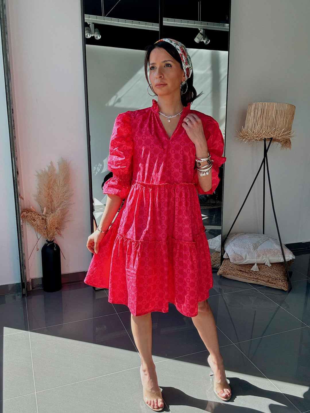 Woman in a red dress standing in a room with a mirror and lamp.