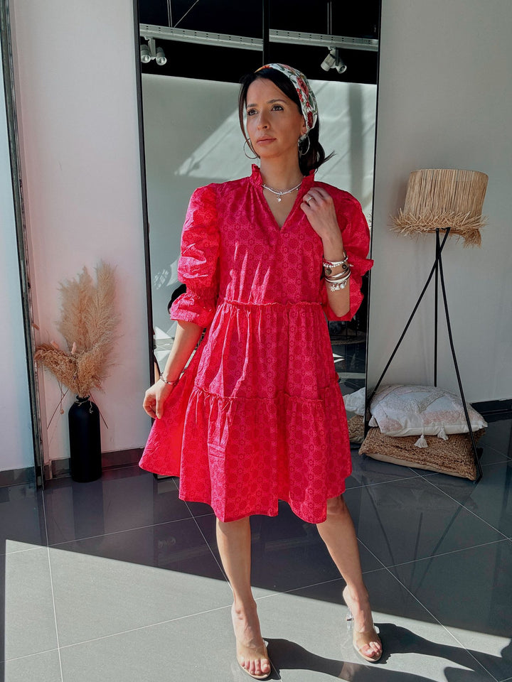 Woman in a red dress standing in a room with a mirror and lamp.