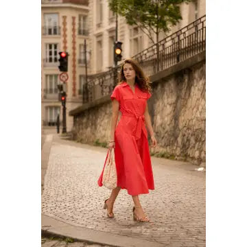 Woman in a red dress walking on a street with traffic lights and buildings in the background.