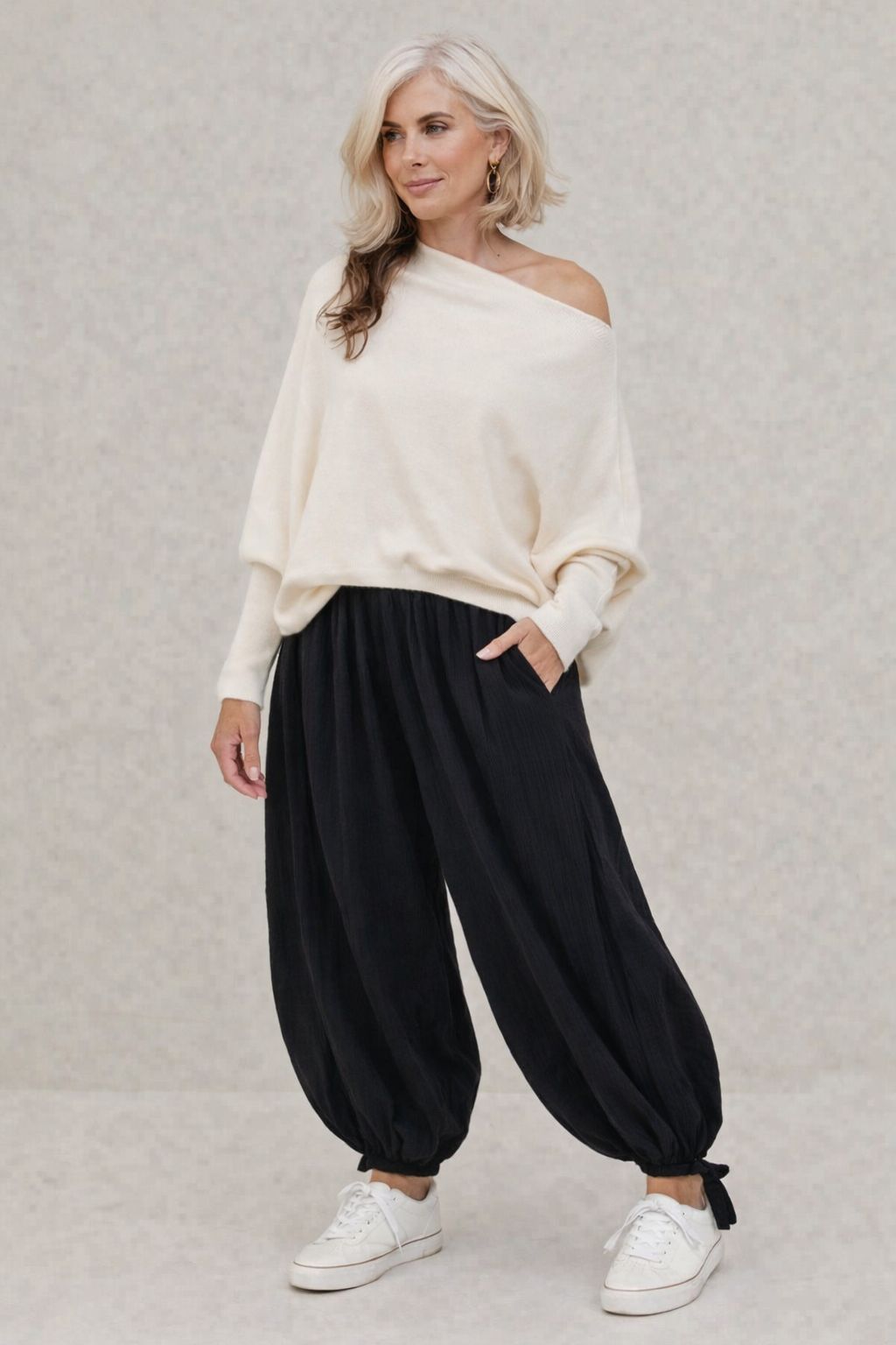Woman wearing a white off-shoulder top and black wide-leg pants on a light gray background