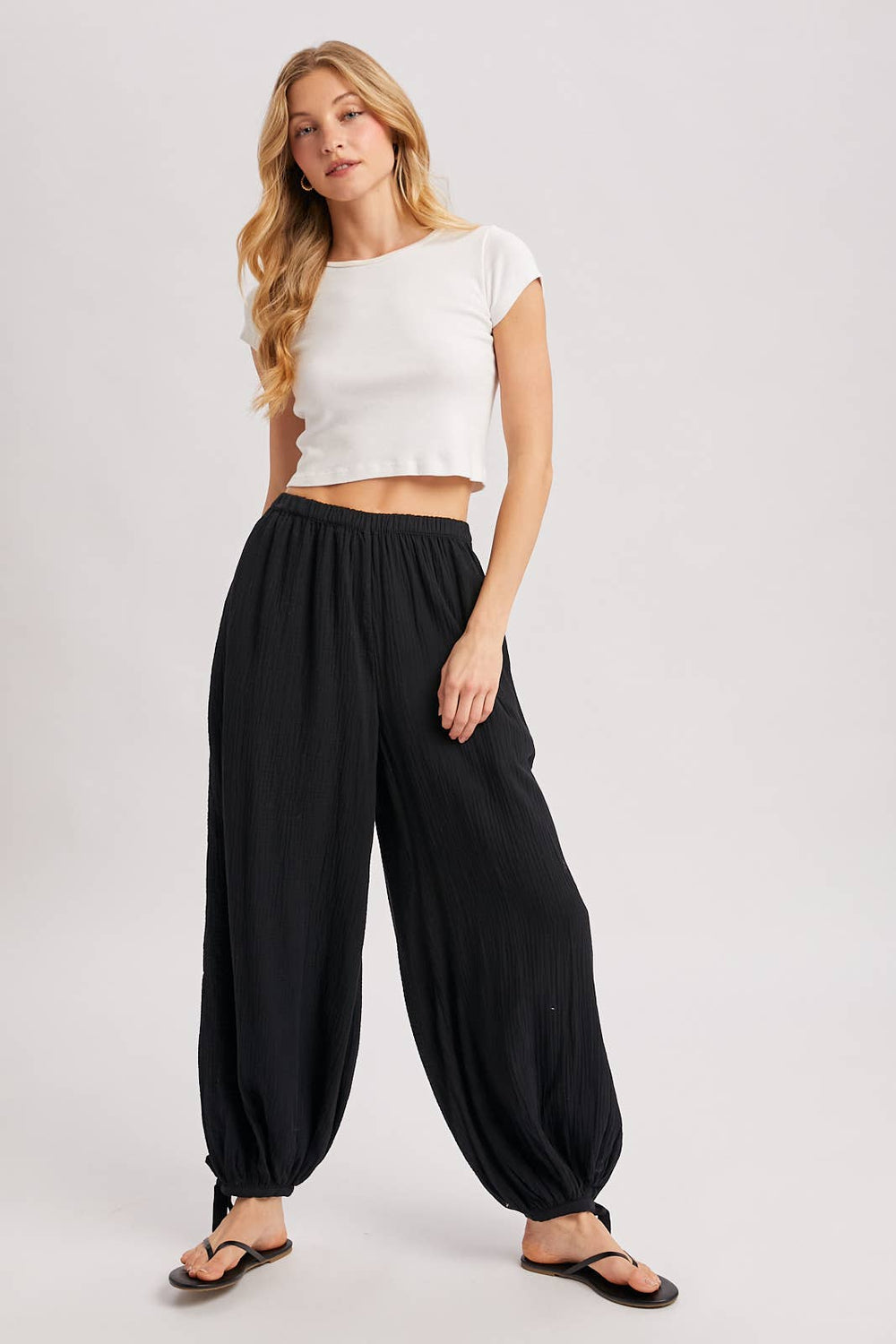 Woman wearing a white crop top and black wide-leg pants on a plain background