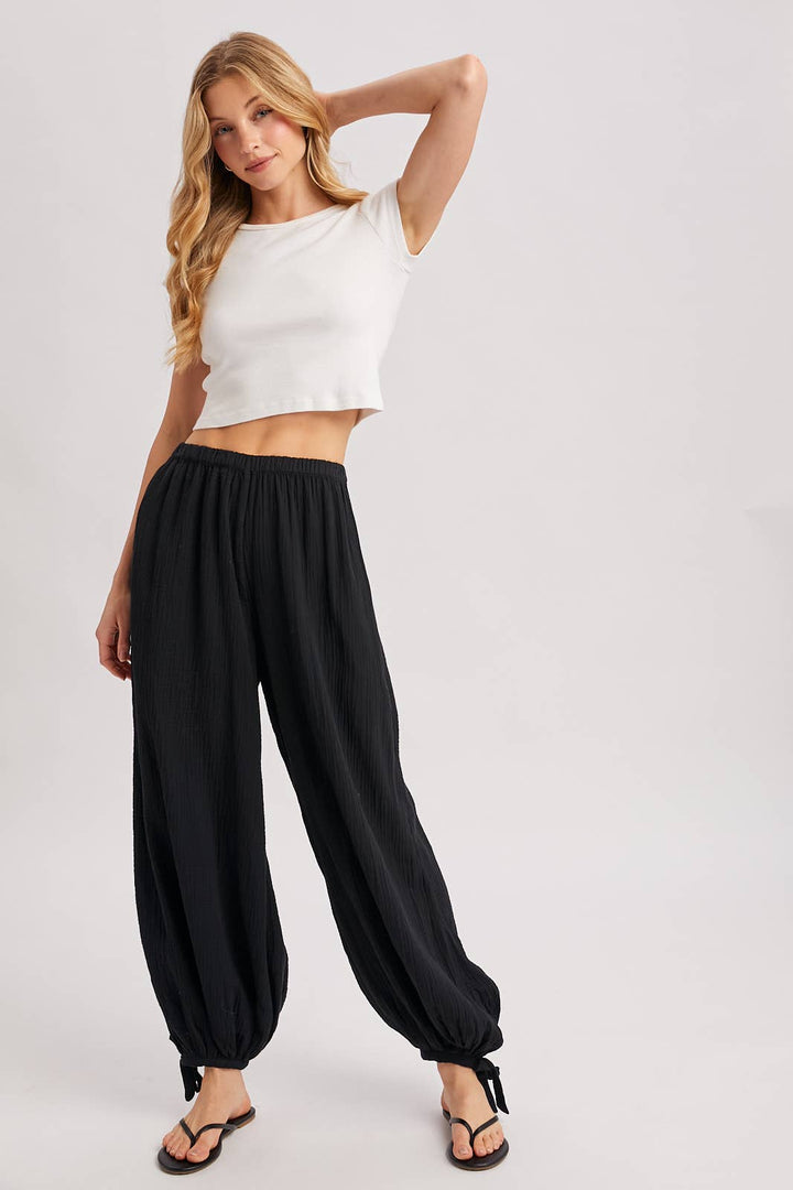 Woman wearing a white crop top and black wide-leg pants on a plain background