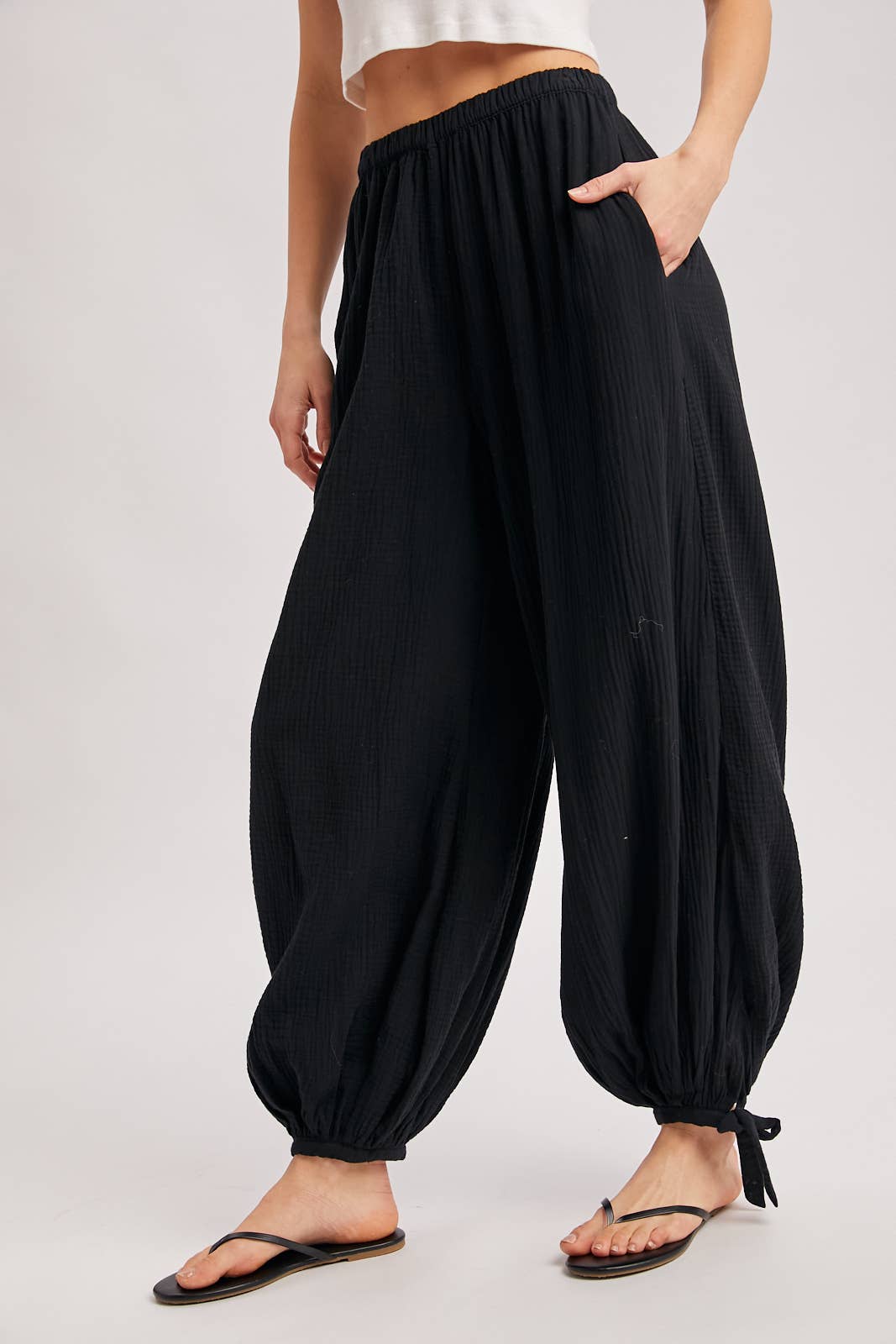 Person wearing black harem pants on a plain background