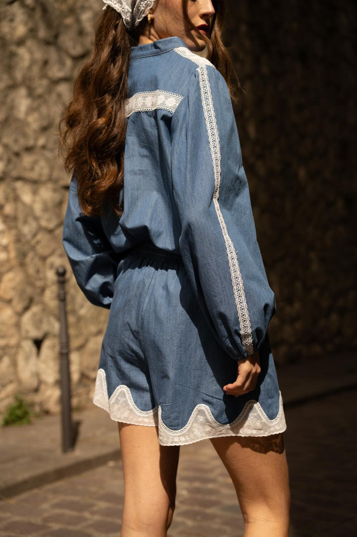 Person wearing a blue outfit with white trim against a stone wall.