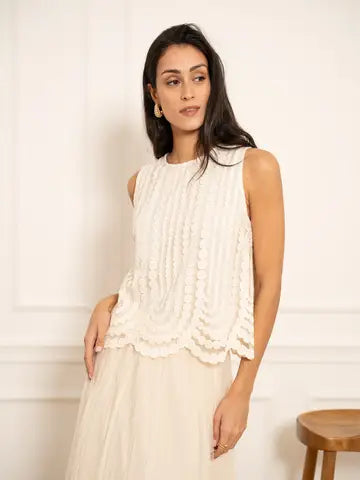 Woman wearing a white sleeveless top with layered ruffles against a plain background
