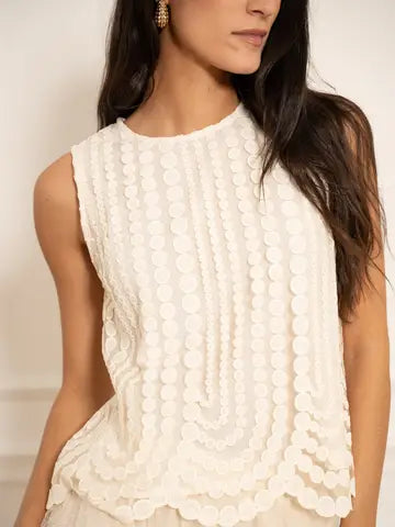 Woman wearing a white sleeveless top with a textured pattern against a neutral background