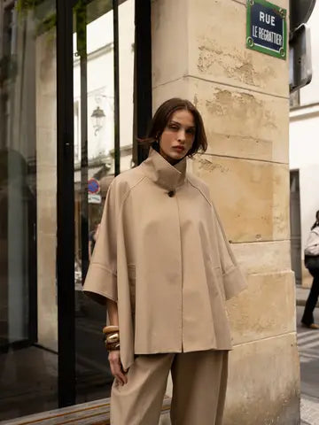Woman wearing a beige cape and pants on a city street.