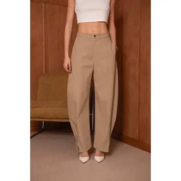 Person wearing beige pants and a white top in a room with wooden paneling.