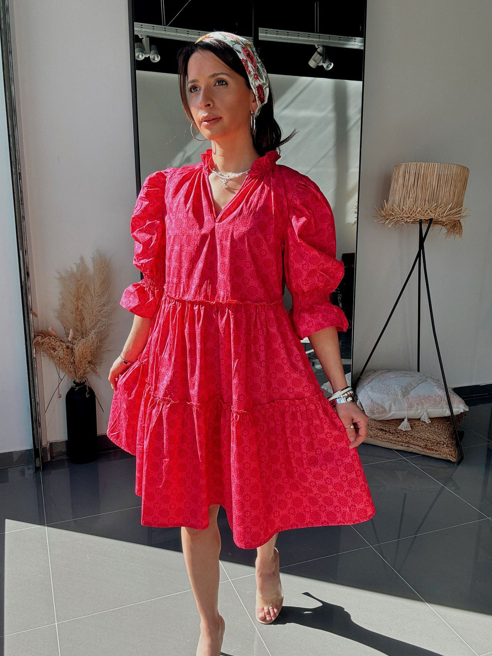 Woman wearing a red dress standing in a room with a mirror and lamp.