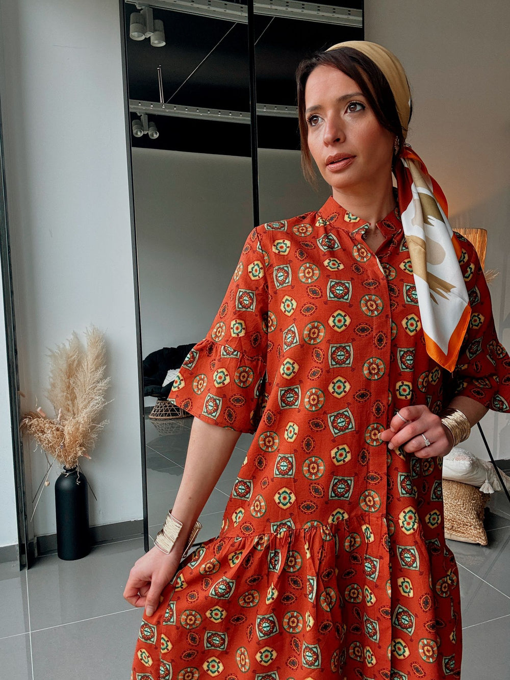 Woman wearing a red patterned dress with a headscarf in a room.