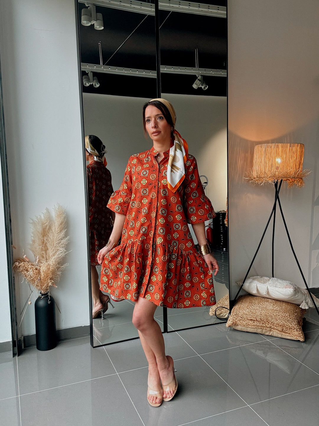 Woman in a red patterned dress standing in front of a mirror in a room with decor elements.
