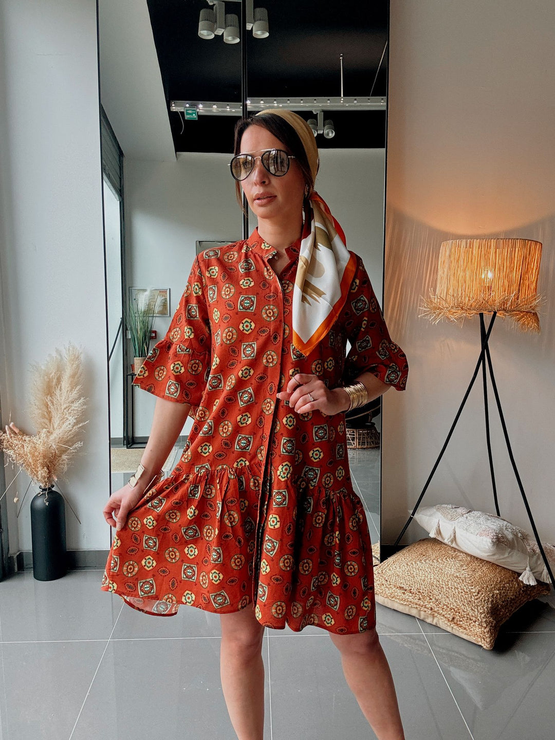 Woman wearing an orange patterned dress with sunglasses indoors.