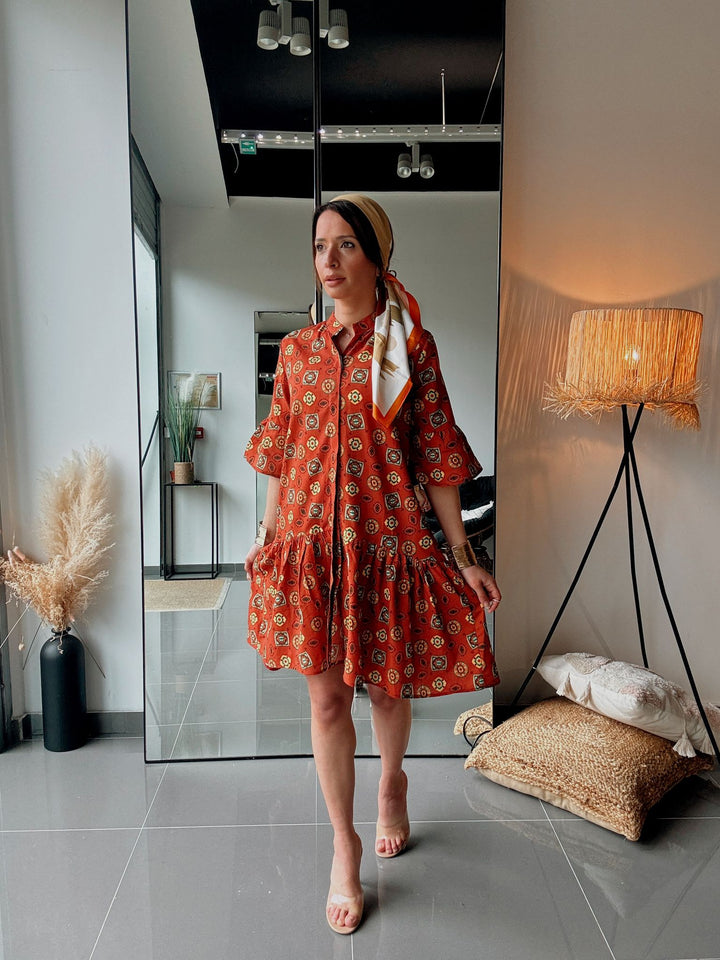 Woman in a red patterned dress standing in a modern interior setting.