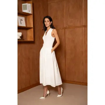 Woman in a white dress standing against a wooden wall.