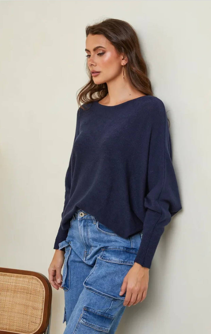 Woman wearing a navy sweater and blue jeans against a beige wall.
